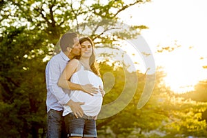 Happy couple in love together in park landscape on sunset with woman pregnant belly and man