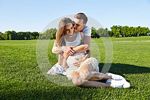 Happy couple in love waiting for child pregnancy hug in the summer park green trees sitting on the grass rest nature husband wife