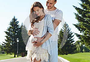 Happy couple in love waiting for child pregnancy hug walk in the summer park green trees nature husband and wife baby boy young
