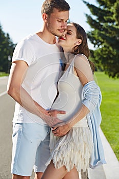 Happy couple in love waiting for child pregnancy hug walk in the summer park green trees nature husband and wife baby boy young