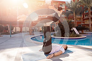 Happy couple lover young woman and man doing balance asana yoga background swimming pool palm trees and sunlight