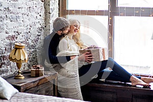 Happy couple of lovers in pullovers give each other gifts sitting photo