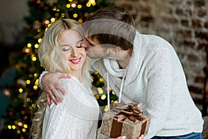 Happy couple of lovers in white pullovers give each other gifts