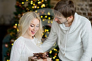 Happy couple of lovers in white pullovers give each other gifts