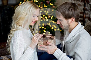 Happy couple of lovers in white pullovers give each other gifts