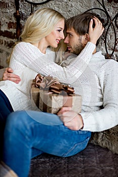 Happy couple of lovers in white sweaters give each other gifts