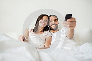 Happy couple lying in bed at home and watching tv