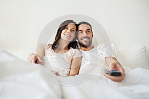 Happy couple lying in bed at home and watching tv