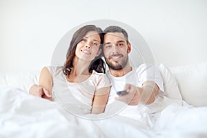 Happy couple lying in bed at home and watching tv