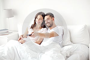 Happy couple lying in bed at home and watching tv