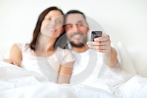 Happy couple lying in bed at home and watching tv