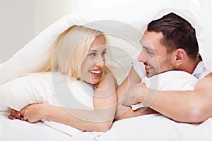 Happy couple lying in bed and talking at home