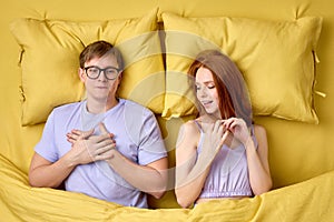 Happy couple lying in bed under duvet after first sex experience, man is surprised by skills of female in bed