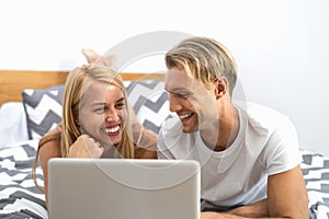 Happy couple lying on bed while using laptop computer - Happy people having funny movie bed time