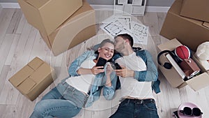 Happy couple lying down on the floor and using smart phone.