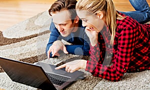 Happy couple lying on the floor with laptop