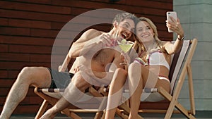 Happy couple making selfie photo with mobile phone near pool.