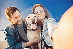 Happy couple making selfie photo with new pet dog retriever Labrador outdoors. Lifestyle summer walk concept