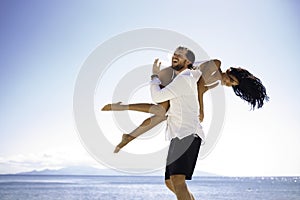 Happy couple, man raised his girlfriend on the shoulder, isolated on beach, blue water, sunny day. Vacantion in Greece.