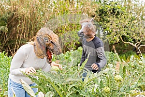 Happy couple man and woman with dinosaur and horse head mask in vegetables garden .Fantasy and humor lifestyle concept