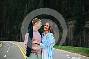 Happy couple man and woman hugging while walking in the mountains against the backdrop of a coniferous forest, smiling and looking