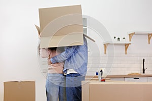 happy couple of man and woman are joking, box on head. moving to new apartment relocation