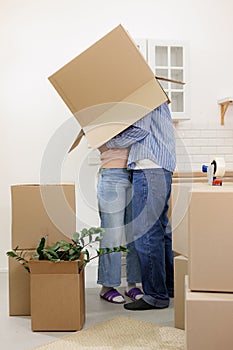 happy couple of man and woman are joking, box on head. moving to new apartment relocation
