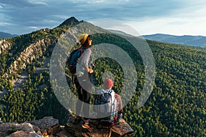 A happy couple in the mountains admires the beautiful views. Travelers enjoy climbing the mountain at sunset. Hiking