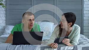 Happy couple networking with digital devices on bed