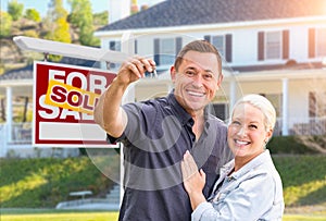 Happy Couple With New House Keys In Front of Sold Real Estate Sign and Beautiful House