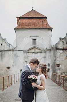 Happy couple of newlyweds posing near castle, fairytale wedding moment beautiful bride and groom hug near ancient castle entrance