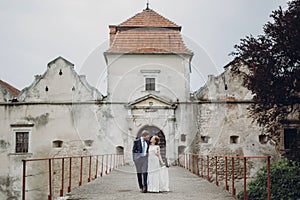 Happy couple of newlyweds walking near castle, fairytale wedding moment beautiful bride and groom hug near ancient castle entrance