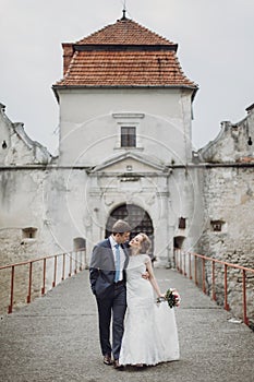 Happy couple of newlyweds walking near castle, fairytale wedding moment beautiful bride and groom hug near ancient castle entrance