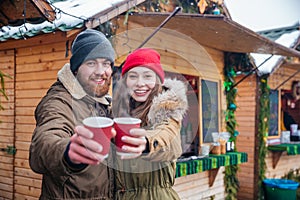 Happy couple offering hot drinks to you on christmas market