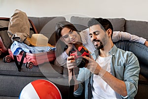 Happy couple packing suitcase and using camera for watching photos in trip. Young spouses preparing for travel