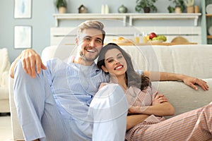 The happy couple in pajamas sitting on the floor background of the sofa in the living room