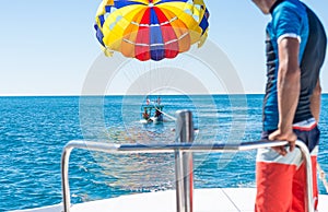 Happy couple Parasailing in Dominicana beach in summer. Couple under parachute hanging mid air. Having fun. Tropical Paradise. Pos