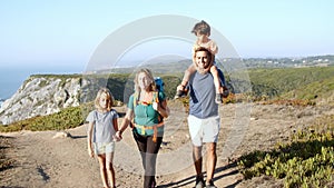 Happy couple of parents and kids walking on path at sea