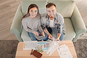 Happy couple with pay bills, calculator and money counting expenses indoors. Money savings concept