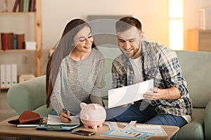 Happy couple with pay bills, calculator and money counting expenses indoors. Money savings concept