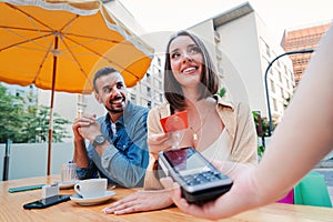 Happy couple paying the bill of the coffee shop using a contactless creditcard payment. Young adult customer woman doing