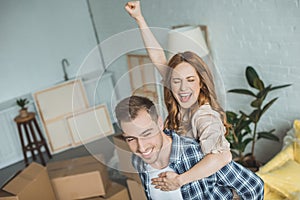 happy couple piggybacking at new apartment with cardboard boxes