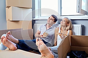 Happy couple with pizza in a new apartment for a housewarming.