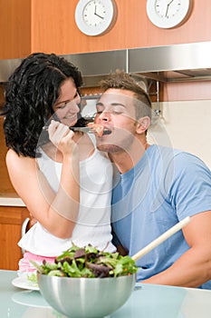 Happy couple playfully eating salad at kitchen