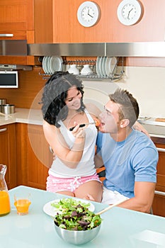 Happy couple playfully eating salad at kitchen