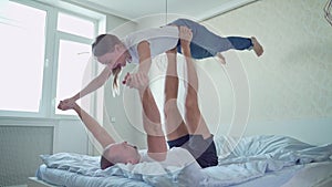 Happy couple playing in bed and having fun. Man lying on bed and lifting his wife with his feet holding her hands.