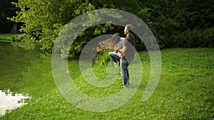 Happy couple is playing outside enjoying spending time together in the park. Strong boy whirls his girlfriend outdoors.