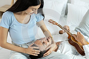 happy couple playing ukulele on bed in bedroom. man and woman enjoying playing music creates happy activities in family. young