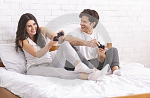 Happy couple playing video games at home, sitting with joysticks