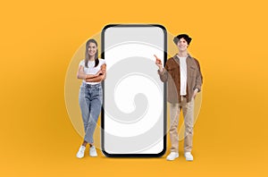 Happy couple pointing at big phone on yellow